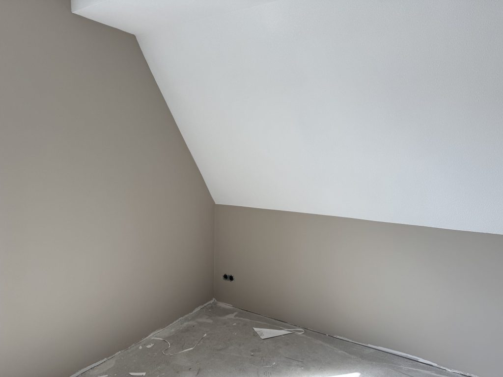 Zolderkamer met een schuine wand en een scherpe knik, afgewerkt in wit en zandkleur